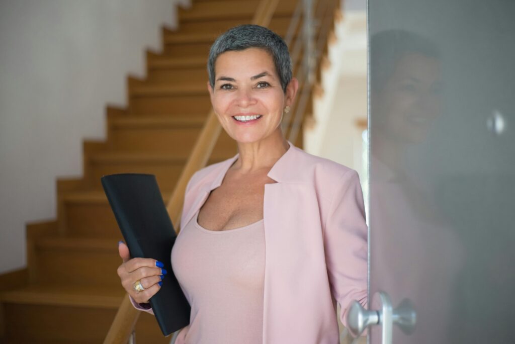 Confident senior woman entering a modern office setting, holding documents and smiling.